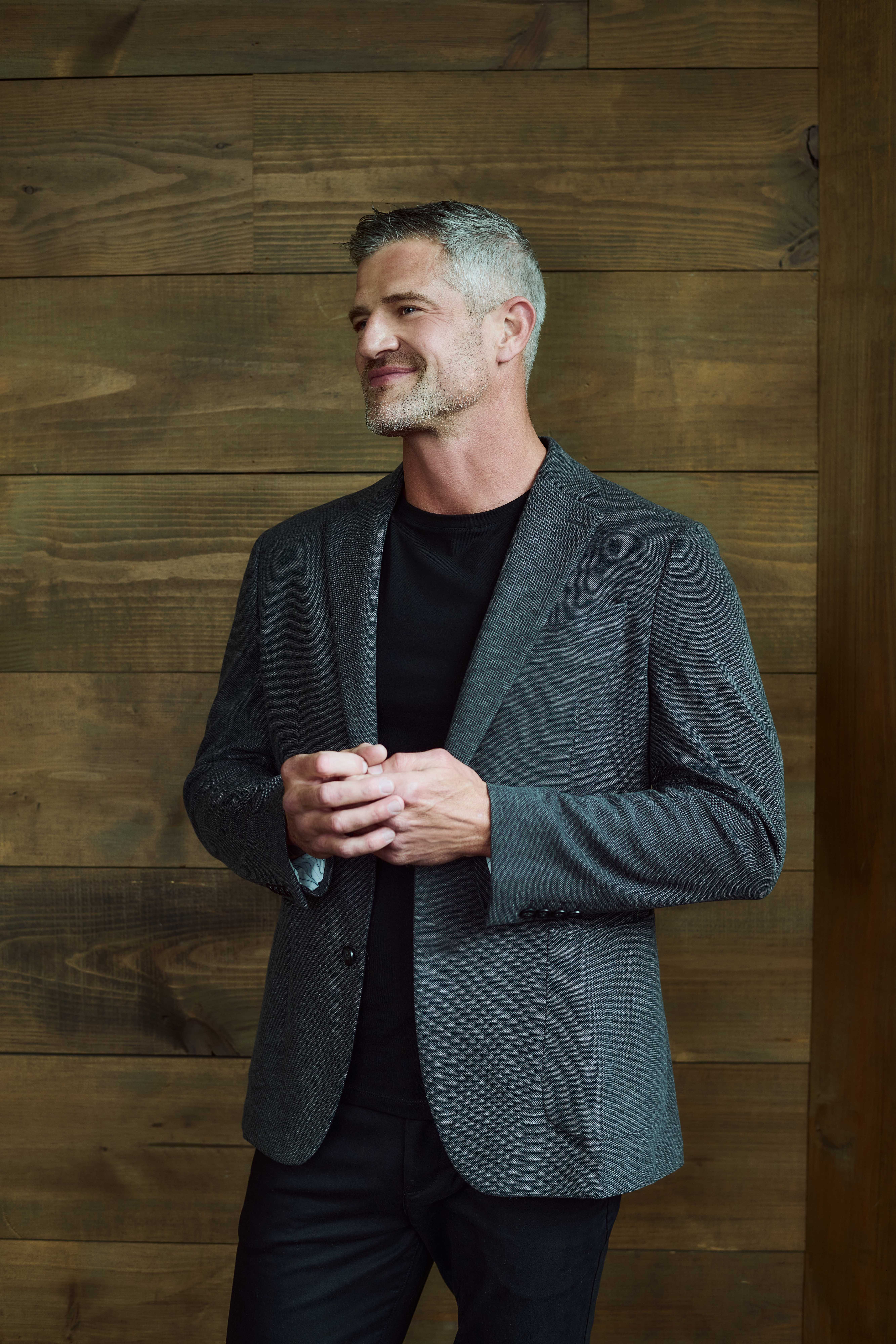 Brandon Burke in a grey blazer against a wood wall